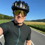 Martin Gratzer smiling on a road bike, wearing a cycling helmet and sunglasses